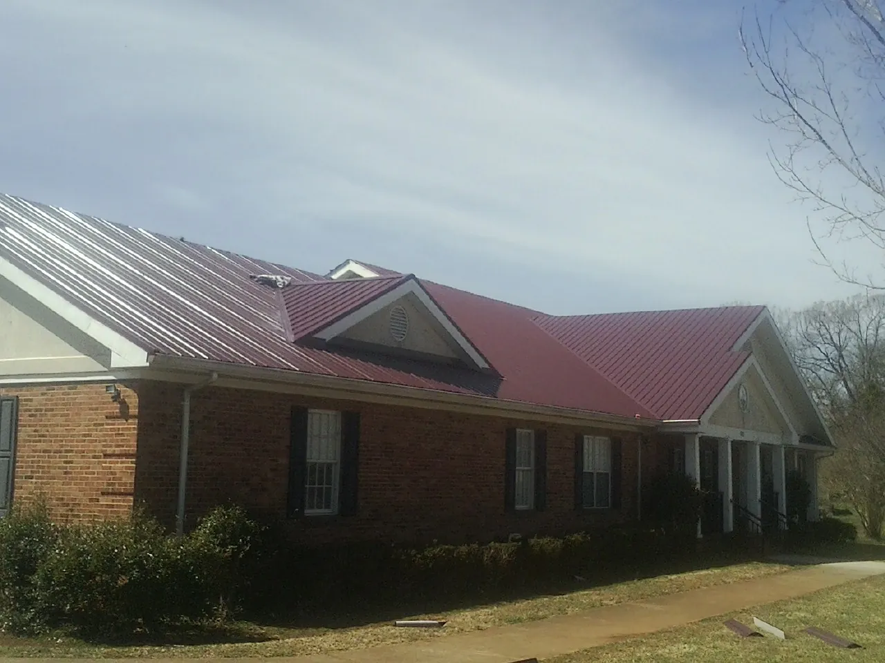 Red metal roof with gabled entries on a long brick building, from a Hail Damage Roof Repair job in Wayland